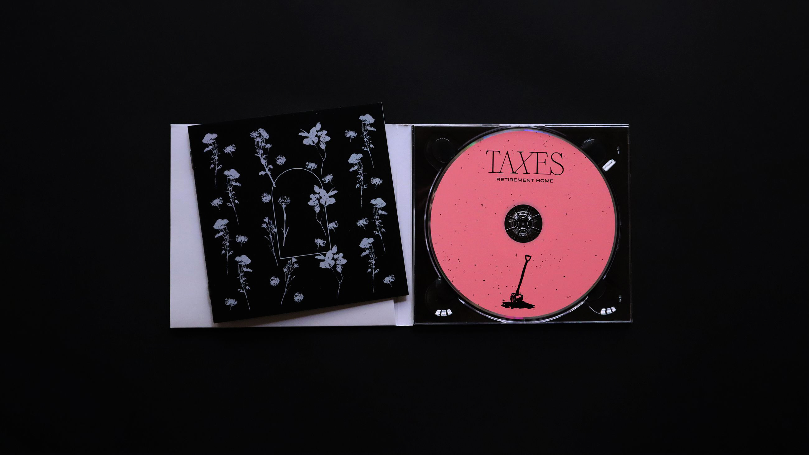 Top-down shot of the CD packaging open: The CD is hot pink and has a shovel illustration on it. The Booklet is a dark navy whith a flower pattern and an arched window graphic in the center. 